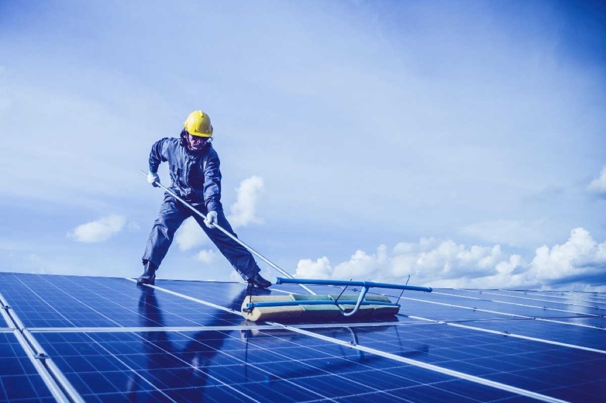 Technicien en casque de sécurité nettoyant des panneaux photovoltaïques avec une brosse télescopique
